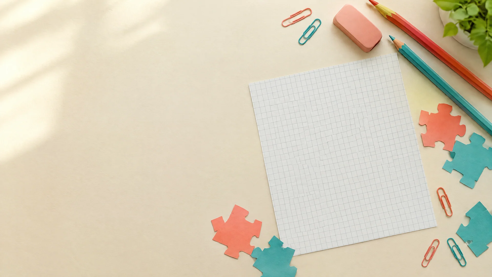 Flat-lay of cream grid paper with coral and teal pencils, paper clips, an eraser and cut-out puzzle pieces